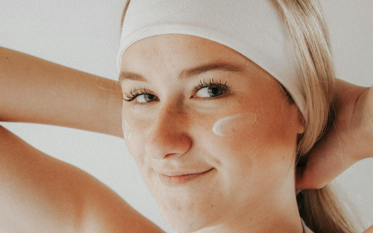 Woman with a white headband smiling, with a smear of cream on her cheek