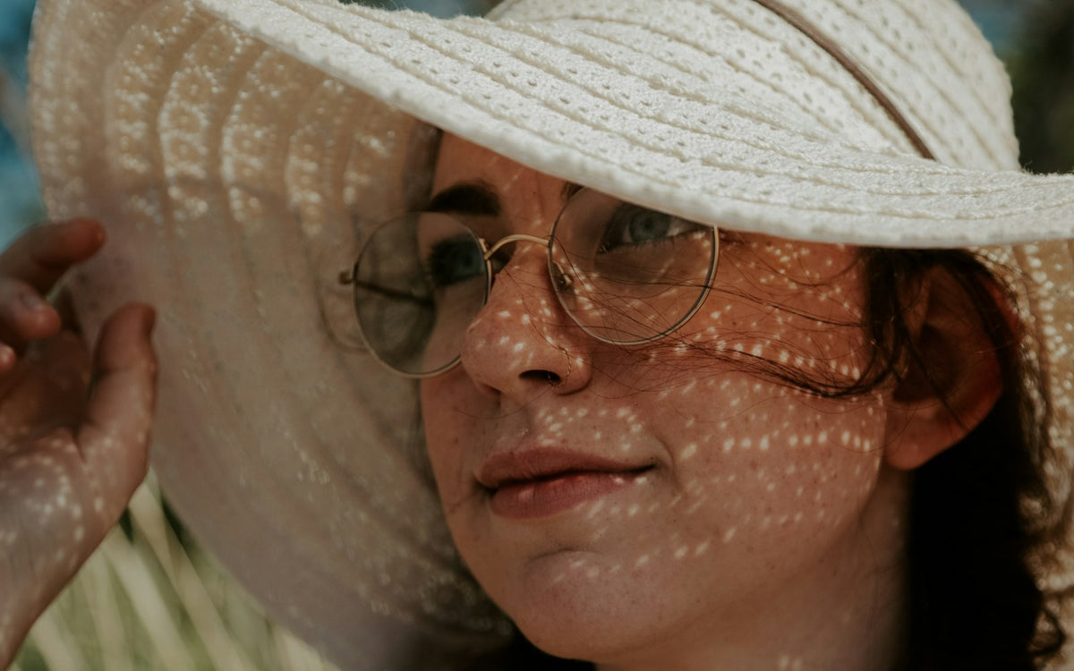 Woman in a white sun hat and glasses with dappled sunlight on her face