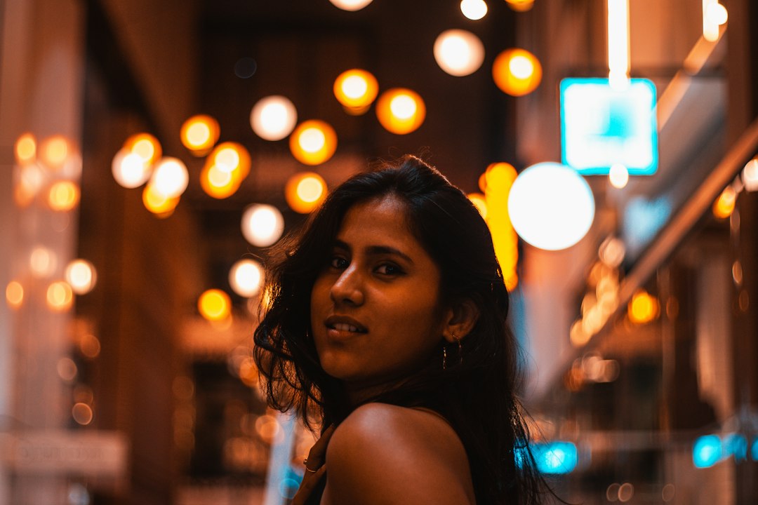 A young Indian woman smiling at the camera in the evening with soft bokeh lights in the background